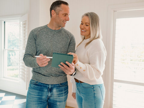 Couple standing in an empty space of their new home planning while looking through the tablet
