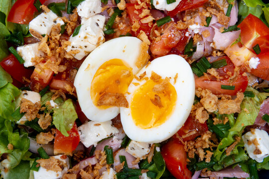 Gros plan sur une salade parisienne avec &oelig;uf mollet, d&eacute;s de jambon, tomates, feta et oignons frits