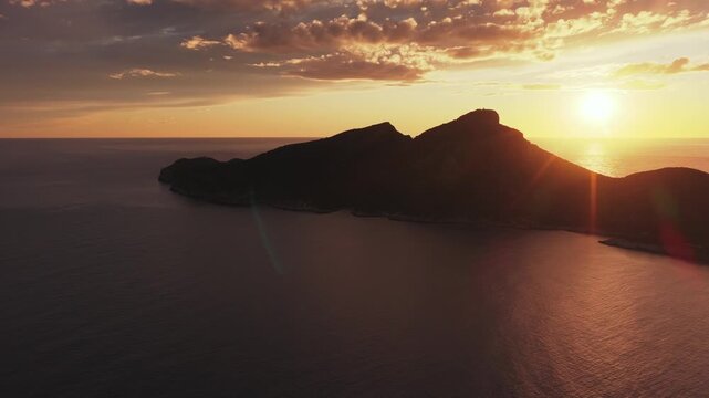 Aerial view of the silhouette of Sa Dragonera island during a golden sunset with calm sea and scattered clouds, Sant Elm, Balearic Islands, Spain.