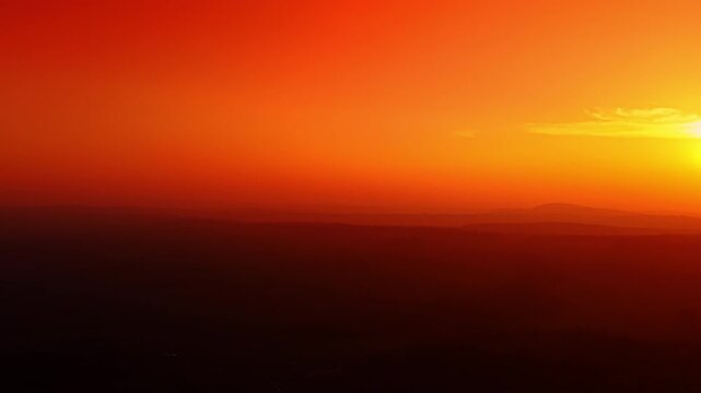 Vivid red and orange sunset over dark silhouetted hilly landscape. Dark rolling hills are silhouetted against a vivid red orange sunset sky in this aerial drone view taken at dusk.