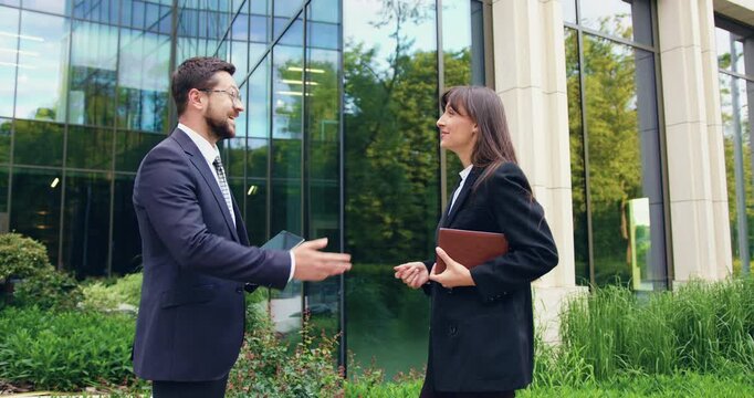 Man and woman having a business conversation outdoors, exchanging a high five after a successful meeting and continuing their workday