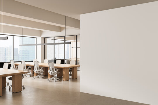 Minimalist open office interior featuring wooden desks, white chairs and a large empty wall for creative mockup poster concept display. 3D Rendering