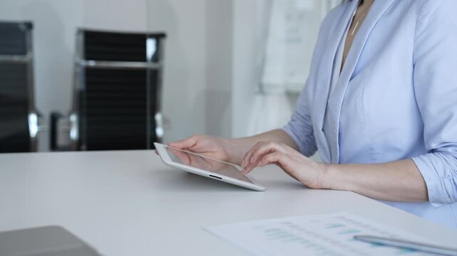 Businesswoman's hands tapping on a digital tablet screen, analyzing data and managing reports in an office environment, embracing technologies for financial planning and professional workflow