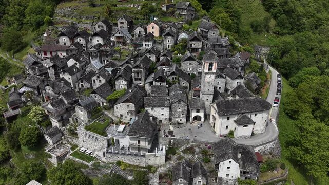 Aerial view of Corippo Albergo Diffuso featuring traditional stone houses and a historic church nestled on a lush green hillside in Corippo, Ticino, Switzerland.