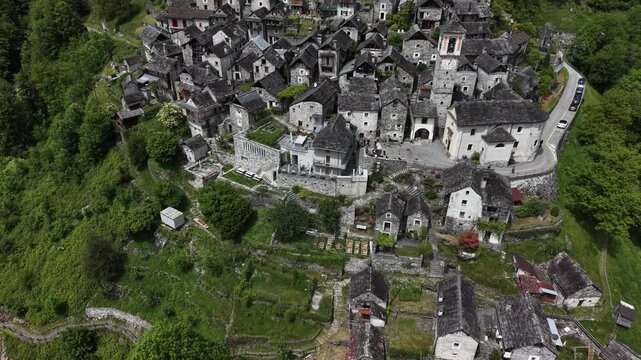 Aerial view of Corippo Albergo Diffuso featuring traditional stone houses and a church tower nestled in the lush green hills of Corippo, Ticino, Switzerland.