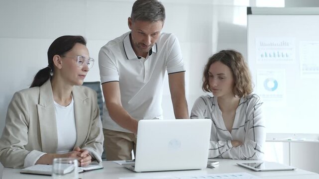 Business team collaborating and analyzing data on a laptop during a dynamic office meeting, uniting efforts to reach shared objectives and drive successful outcomes together