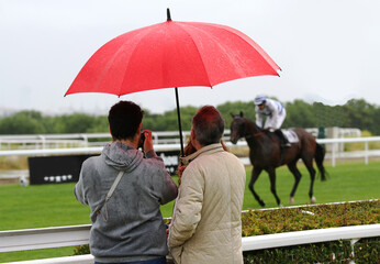 Paraguas en hipódromo con espectadores de caballo de carreras y lluvia en plan de ocio © Diego