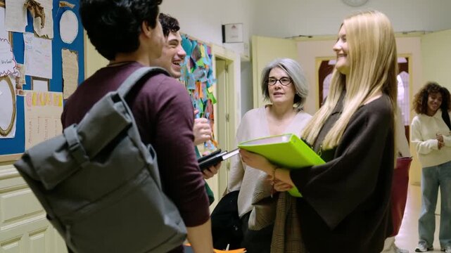 Young students talking with a female professor in a busy high school corridor during a class break