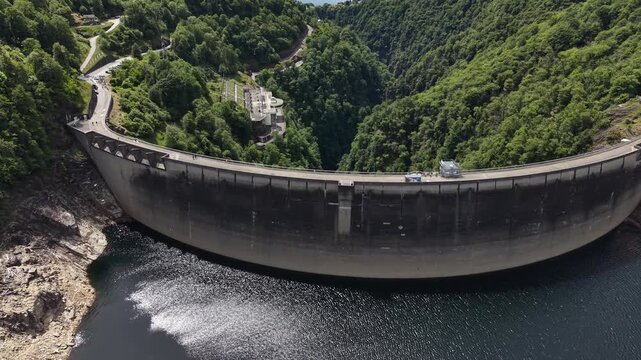 Aerial view of the Verzasca Dam surrounded by lush green mountains and the valley landscape in Gordola, Ticino, Switzerland.