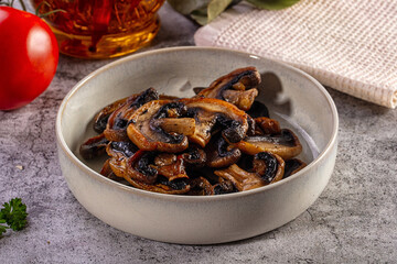 Fototapeta premium A rustic ceramic bowl of sauteed or grilled sliced mushrooms on a stone table