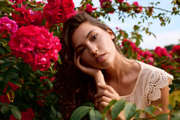 Naklejka premium Enchanting young woman embraces the beauty of nature amidst blooming roses in a sunny park