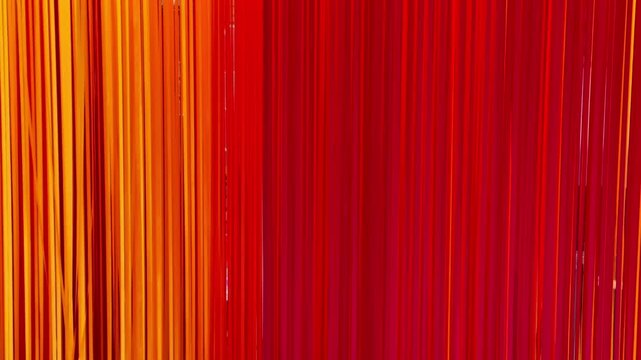 Abstract background of vertical colorful hanging ribbons in warm tones of red, orange, and yellow.