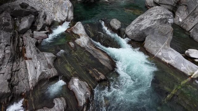 Aerial view of Verzasca river in Valle Verzasca with turquoise water flowing over striped rocks in Verzasca, Ticino, Switzerland.