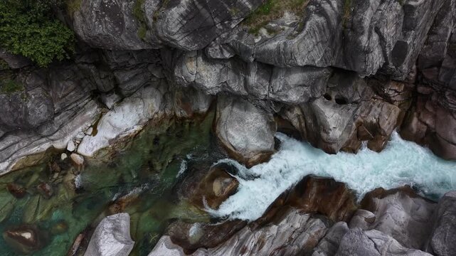Aerial view of the crystal clear turquoise water of Valle Verzasca flowing through smooth grey boulders and rocky riverbed in Verzasca, Ticino, Switzerland.