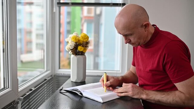 mature man reading book and highlighting text near apartment window at Full home HD video