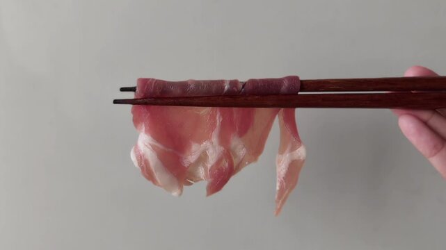 Thinly sliced pork neck for shabu-shabu, with chopsticks lifting the pieces. white background