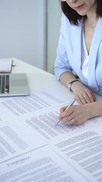 Businesswoman signing legal document on an office desk, reviewing terms of a contract or agreement before endorsing it, completing an important corporate transaction