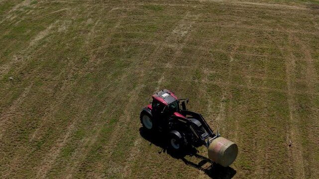 Tractor Harvesting Hay: A powerful tractor operates in a vast, sun-drenched field, collecting a large bale of hay, embodying the essence of agricultural labor and rural life.