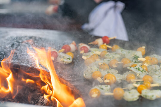 Brochettes de Saint-Jacques et tomates en cuisson sur brasero avec flammes et fum&eacute;e lors d&rsquo;un barbecue en ext&eacute;rieur.