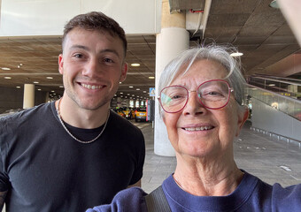 Smiling Senior Woman and Young Man Taking Selfie in Busy Airport Pickup Terminal © luciano