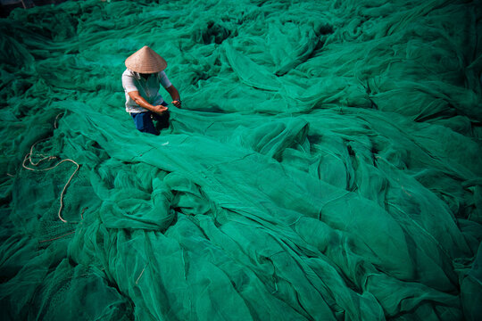 Vietnamese traditional craft fisherman sorting green nets outdoors in hat