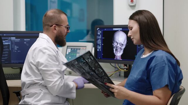 Doctor explains brain scan on computer to nurse in radiology department, concept of MRI diagnosis, medical teamwork and healthcare analysis.