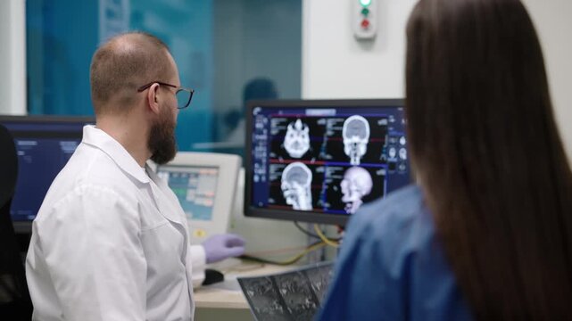 Doctor points at brain scan on screen during radiology review with nurse, showing MRI diagnostics, healthcare technology and medical expertise.