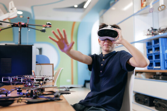 Portrait happy Teen boy wearing virtual reality headset reaching in workshop with drone design