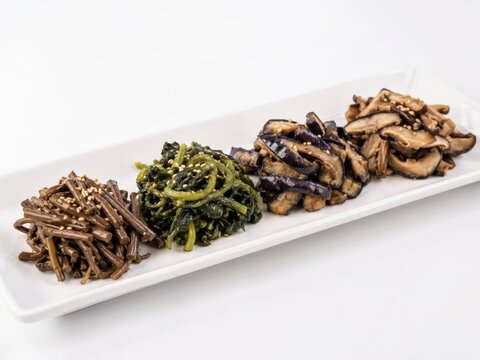 Jinchae or boreum namul presented on a long white rectangular tray separated rows of seasoned dried fern stems dried radish greens dried eggplant and mushrooms clean tasting menu composition