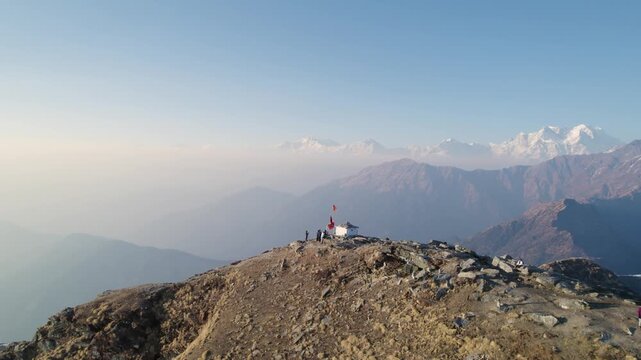 Aerial view of Shri Tungnath Temple with people on the rocky peak and Himalayan mountains in the background in Rudraprayag, Uttarakhand, India.
