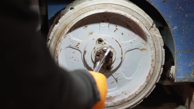 Mechanic using adjustable pliers to repair or maintenance a heavy duty industrial cart wheel in a workshop factory setting, focusing on manual labor and manufacturing business
