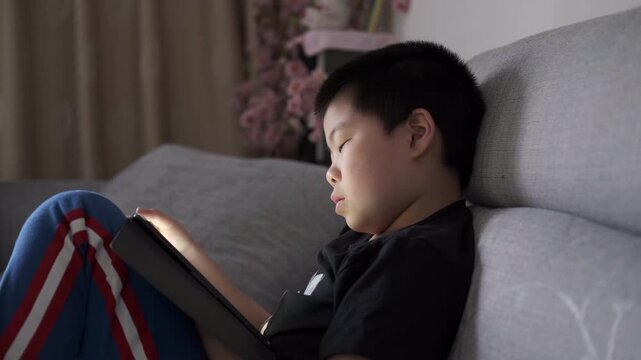 Chinese Child Using Tablet at Home Highlighting Education and Screen Addiction Themes