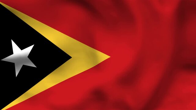 National flag of Timor-Leste on wavy textile. Features a red field with overlapping black and yellow triangles and a white star. Top-down view for independence day and Southeast Asian news themes.