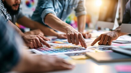 Obraz premium Group of diverse individuals examining color swatches and design samples on a table in a bright, modern workspace with creative elements in the background