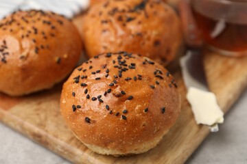Naklejka premium Freshly baked buns with sesame seeds, butter and tea on light grey table, closeup