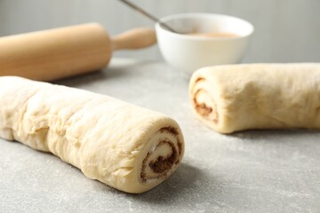 Fototapeta premium Raw cinnamon roll dough on grey textured table, closeup