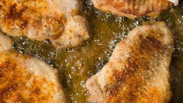 Close up of pork chops frying in hot bubbling oil. Top down macro of seasoned meat cutlets sizzling on a pan with crispy golden crust.