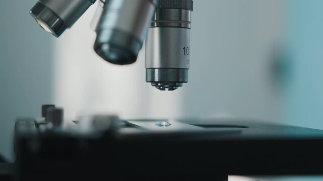 Microscope objective lens lowering onto glass slide for scientific analysis
