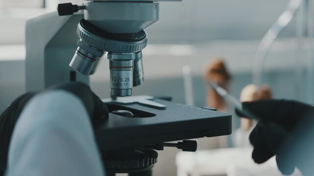 Laboratory technician placing microscope slide under objective lens