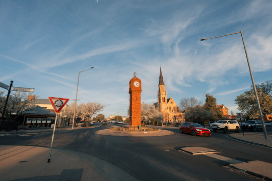 Traffic passing through roundabout in small town with clock tower and church spire under a wispy sky