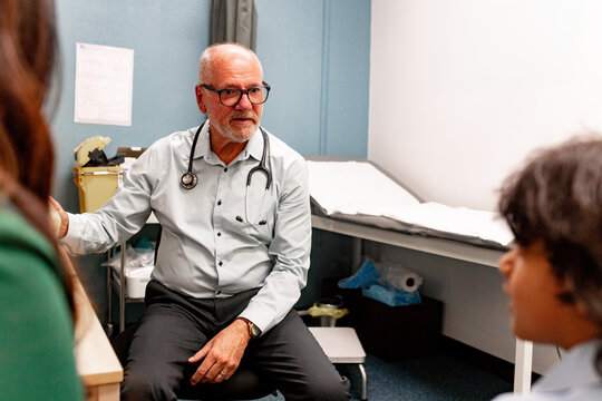 Male doctor talking to a child patient with a guardian present in the clinic