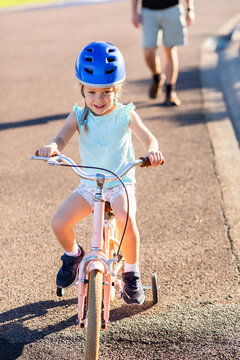 Happy young Australian kid riding her bike on quiet suburban road with parent following