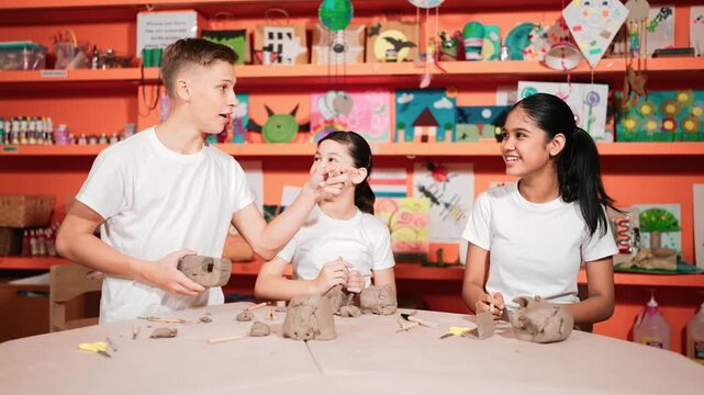 Smart boy pick clay while looking though hole at pottery workshop.Skilled diverse high school student working and modeling dough while laugh at happy child at art lesson. Creative art. Edification