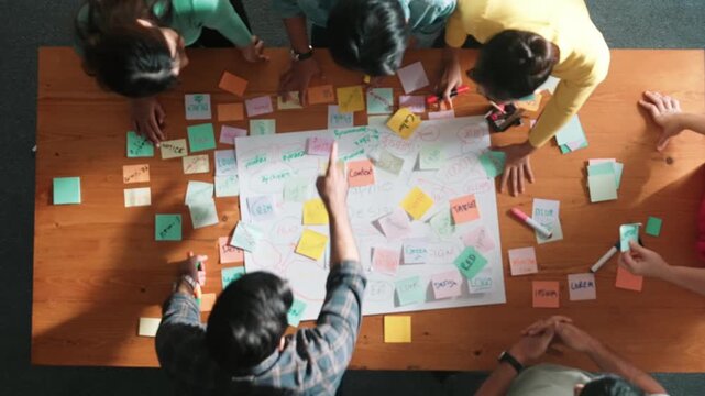 Top view of project manager writing and sticking stick notes. Aerial view of professional business people working together planning strategy while drafting mind mapping at meeting room. Symposium.