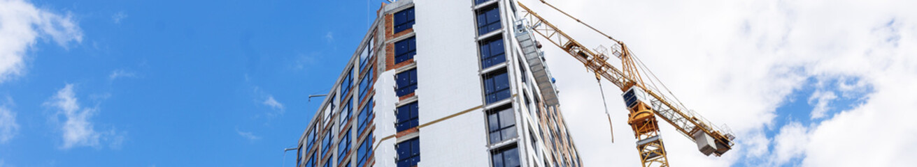 Panoramic view of residential tower construction with crane and blue cloudy sky. Banner for website © Olha Tsiplyar