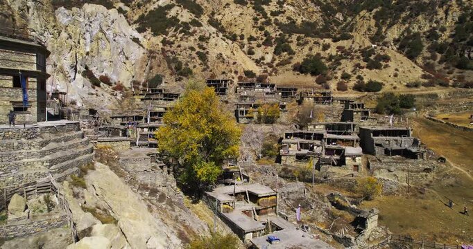 An aerial view of a traditional Himalayan stone village clinging to a steep dry hillside in Nepal.