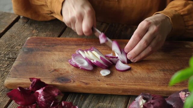 Hands slice red onion on wooden board. Cooking food process, meal prep. 