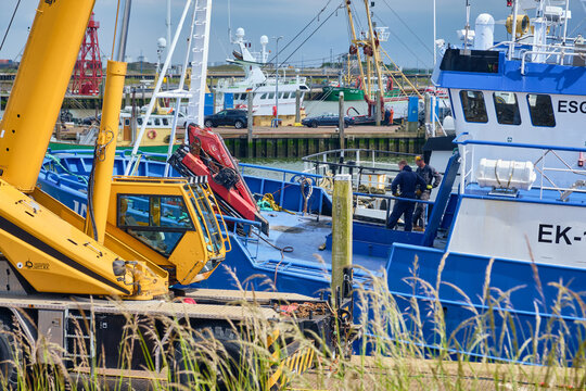 Den Oever, Netherlands - 18 May 2026: View of British fleet vessels being renovated at the Machinefabriek fishing repair wharf with a large yellow crane and workers in the harbor.