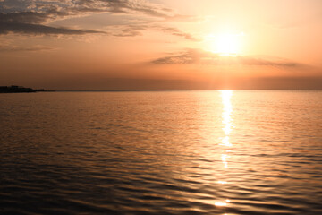 Obraz premium Sunset over calm ocean with warm orange colors reflecting on water surface. peaceful scene, sense of tranquility and nature beauty. Beautiful sunset on calm sea.golden sunlight shimmering across water
