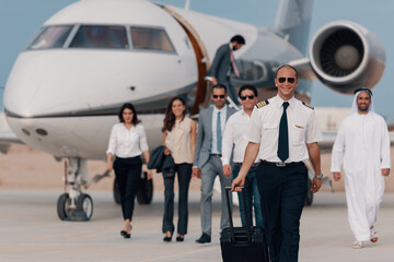 Pilot leading business executives and diverse passengers from private jet on tarmac after luxury flight © .shock